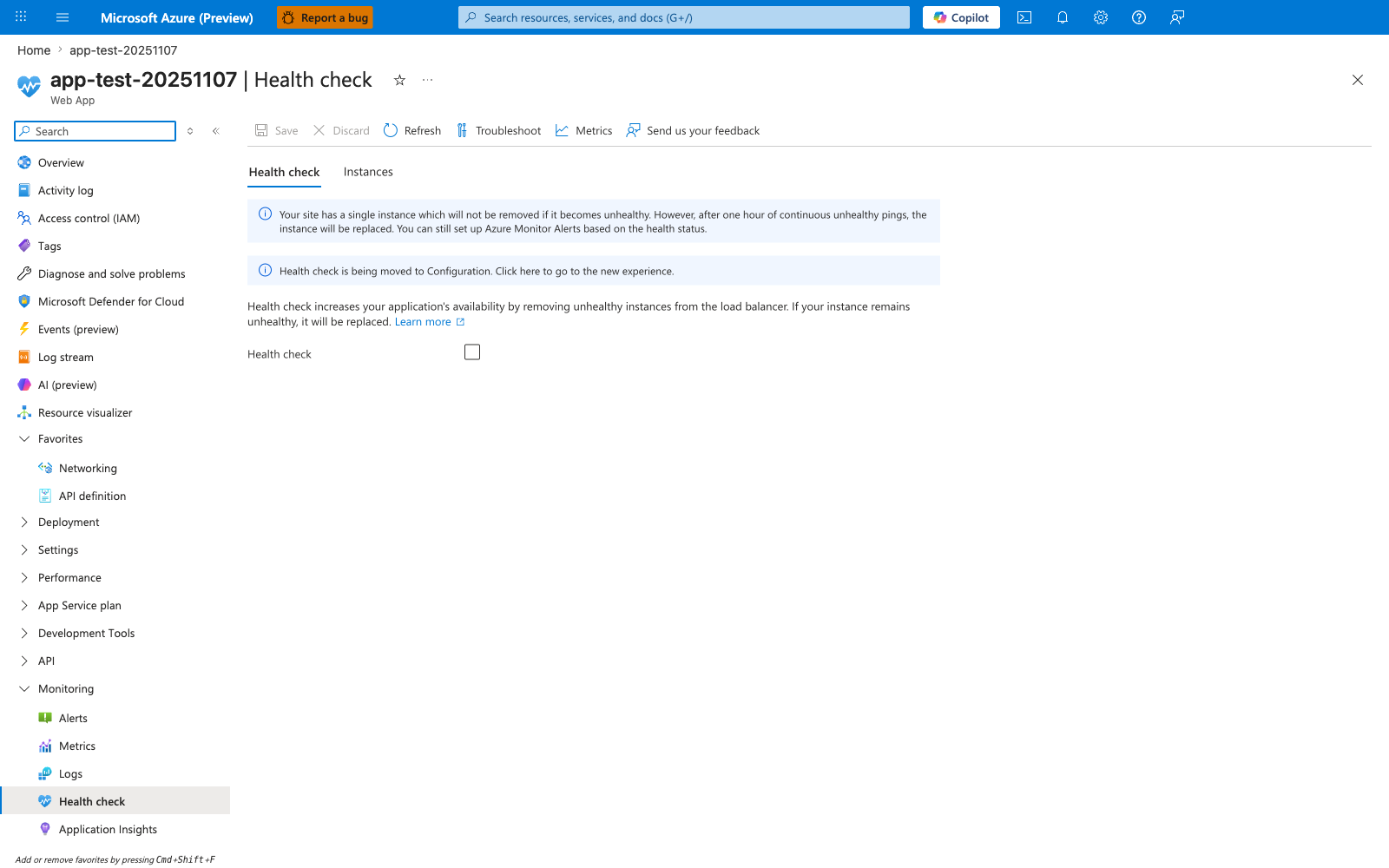 Azure portal Health check blade for app-test-20251107 with tabs Health check (active), Instances; toolbar buttons Save, Discard, Refresh, Troubleshoot, Metrics, Send us your feedback; info banner reading "Your site has a single instance which will not be removed if it becomes unhealthy. However, after one hour of continuous unhealthy pings, the instance will be replaced. You can still set up Azure Monitor Alerts based on the health status."; second info banner reading "Health check is being moved to Configuration. Click here to go to the new experience."; description text "Health check increases your application's availability by removing unhealthy instances from the load balancer. If your instance remains unhealthy, it will be replaced." followed by a Learn more link; a single Health check toggle row with the checkbox in the unchecked state; left service navigation showing Overview, Activity log, Access control (IAM), Tags, Diagnose and solve problems, Microsoft Defender for Cloud, Events (preview), Log stream, AI (preview), Resource visualizer, expanded Favorites with Networking and API definition pinned, and an expanded Monitoring group with Alerts, Metrics, Logs, Health check (selected), Application Insights.